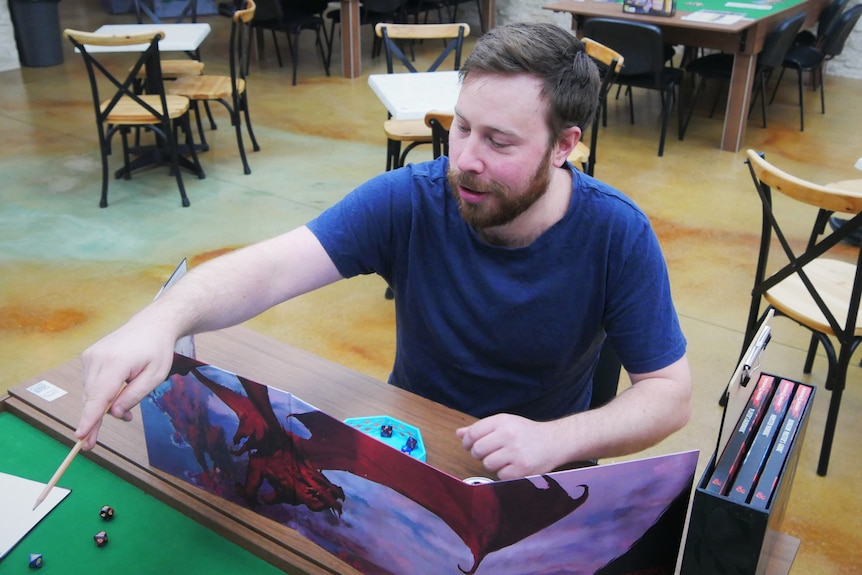 A man sits at a table, he is animatedly pointing out of frame in the middle of a role playing game