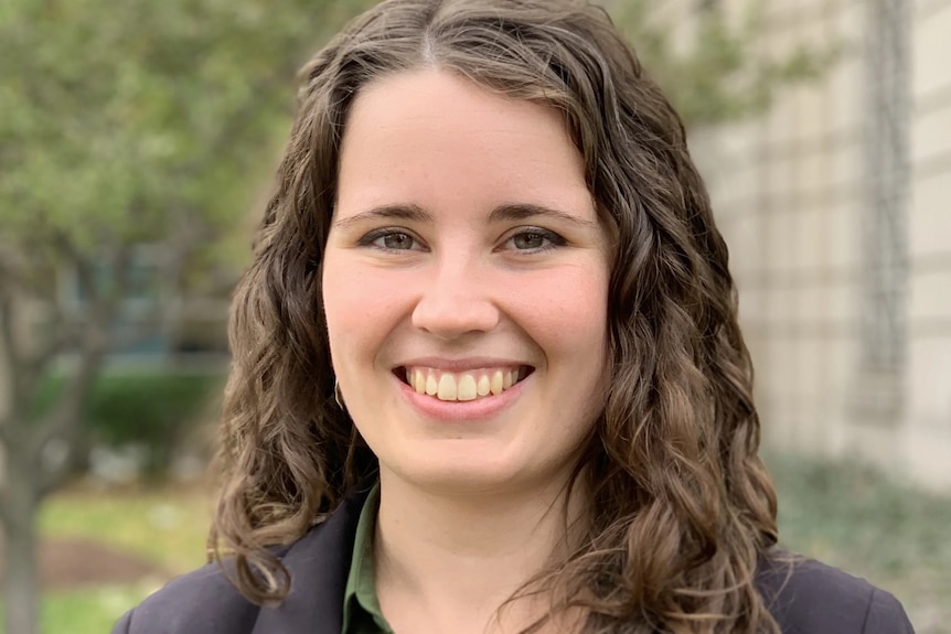 A young woman wearing a black blazer over a green shirt, smiling