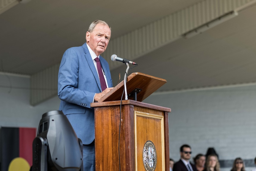 A man in a suit and tie speaking into a microphone at a podium.  