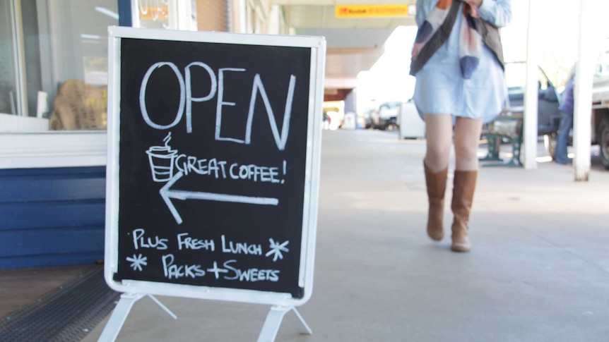 A blackboard advertising a coffee shop as a young woman walks past in cowboy boots.