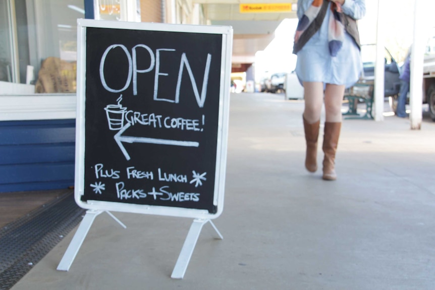 A blackboard advertising a coffee shop as a young woman walks past in cowboy boots.