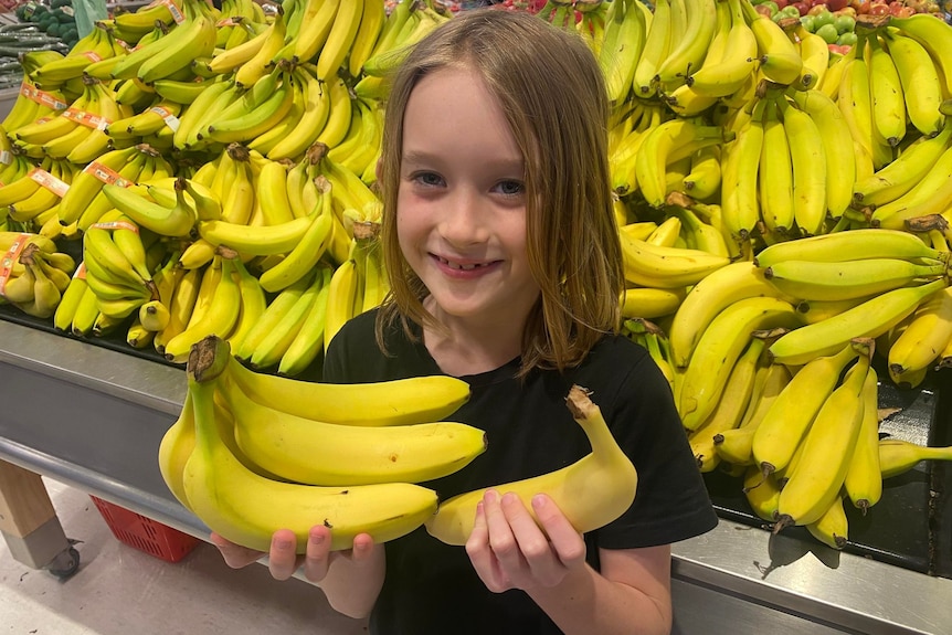 Travis Stewart stands in front of bananas at the supermarket holding bananas in both hands