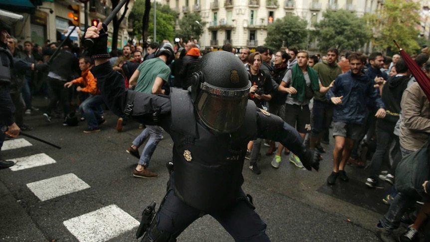 Un poliziotto alza il testimone davanti ai manifestanti a Barcellona