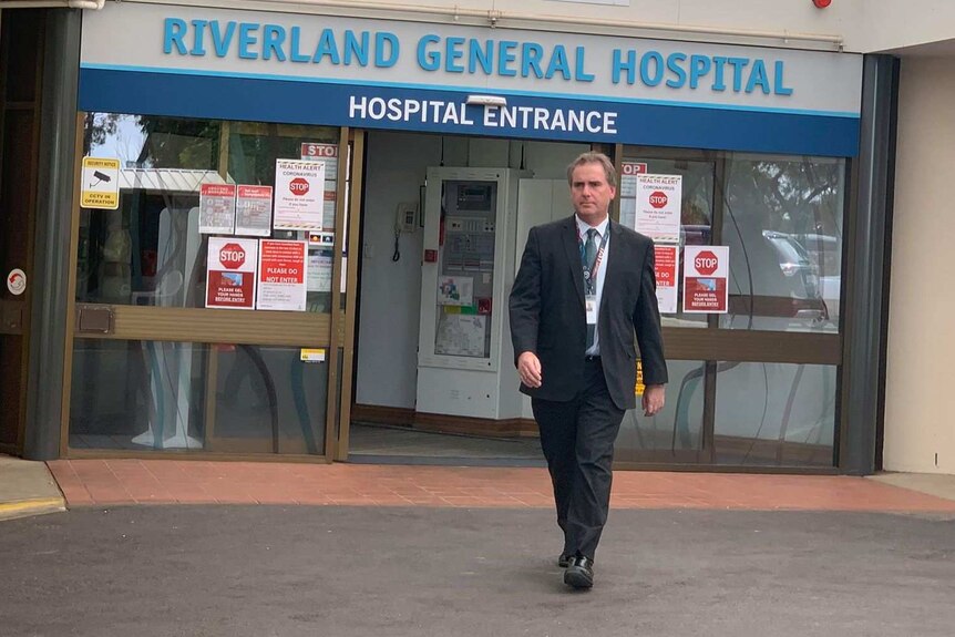 A man walking outside the entrance of a hospital.