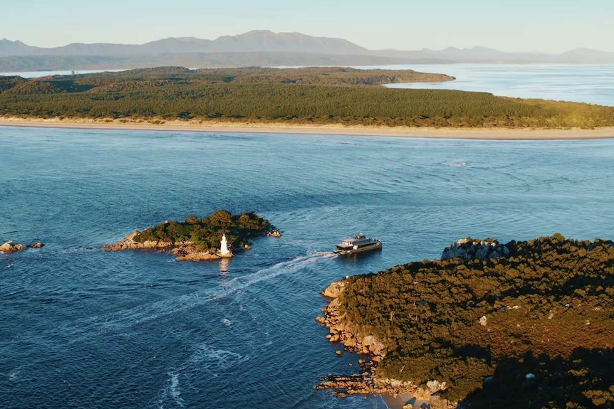 A passenger craft passes through a narrow channel of water at the mouth of a river.