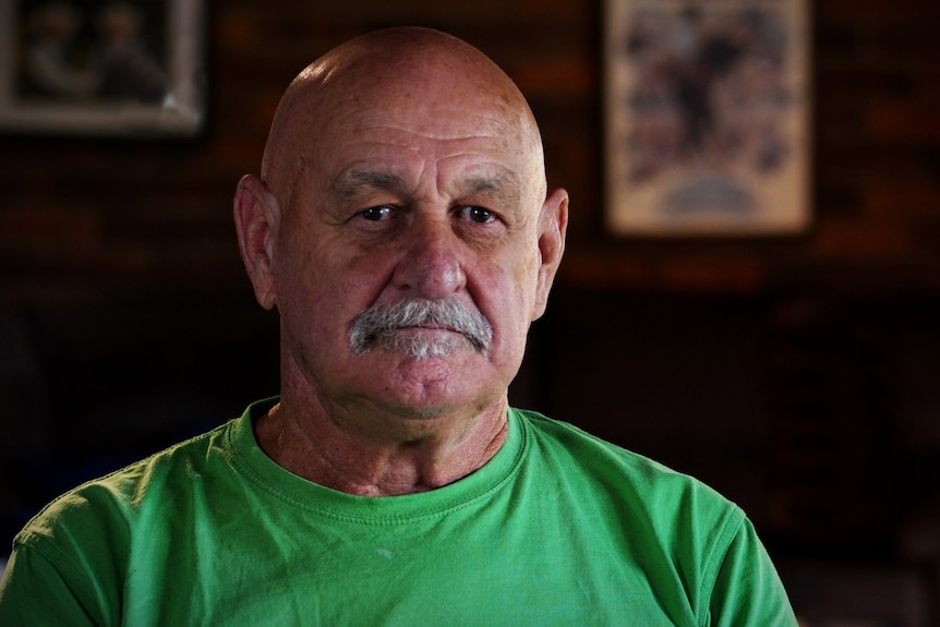 A man with a grey moustache wearing a green shirt.