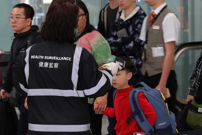 a woman points a device as people walk past her at an airport