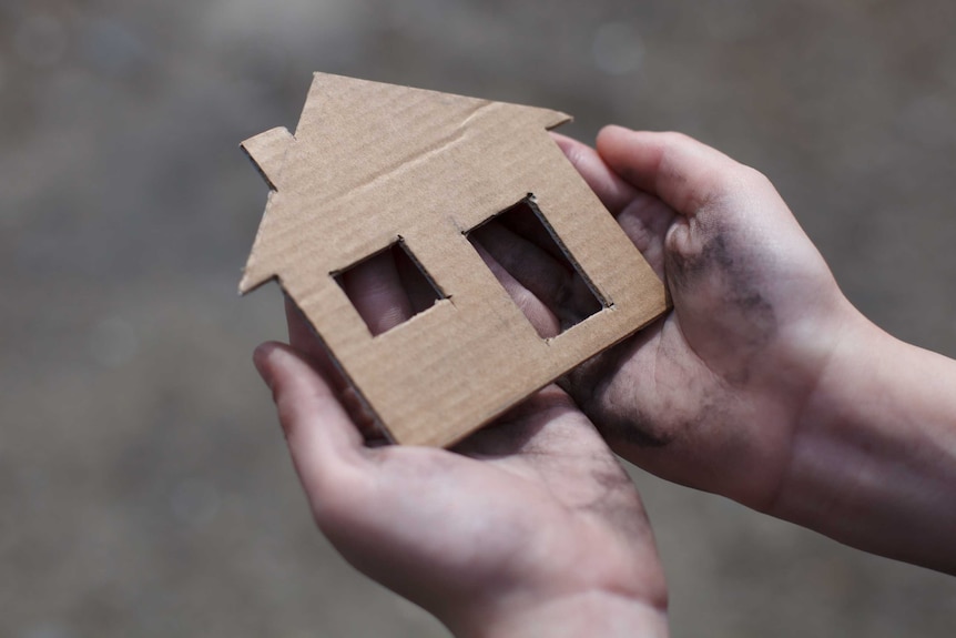 Hands holding a cardboard house.