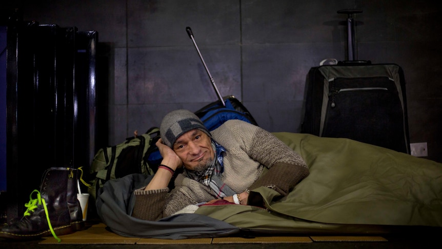 A homeless man lying on his side in a swag, looking at the camera smiling
