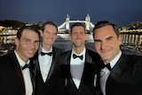 Four men in tuxedos pictured in front of tall bridge.