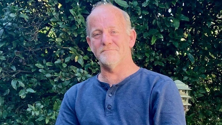 man in blue shirt sitting in front of a bush