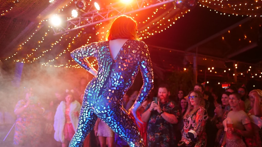 A drag queen wearing a colourful leotard, photographed frokm behind