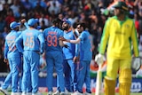 The Indian players congregate to celebrate. In the foreground and out of focus, Usman Khawaja walks off the field.