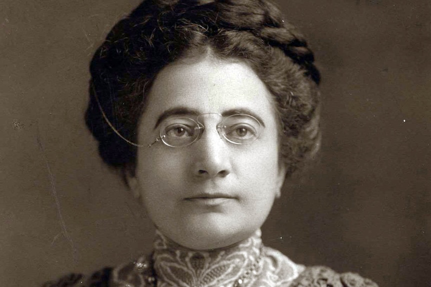 A woman with glasses perched on her nose sits for a black a white portrait, c. 1912.