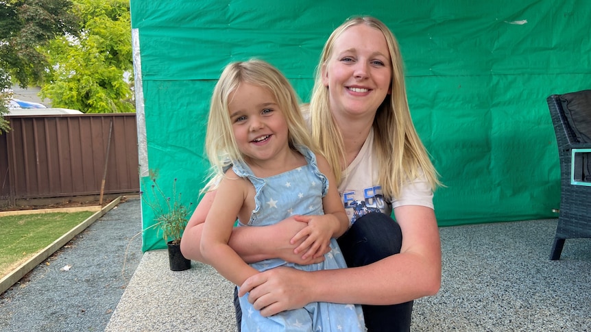 Mother and daughter crouching down, cuddling, posing for photo outside