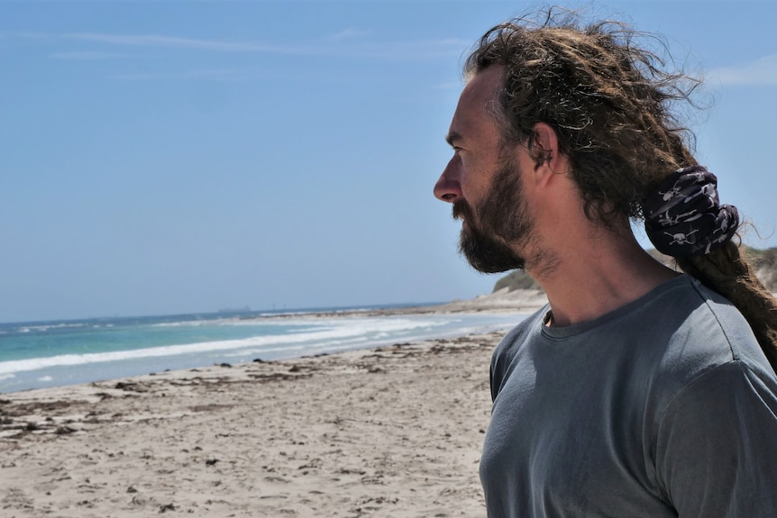 Man standing facing the ocean in Geraldton, blue sea and sand