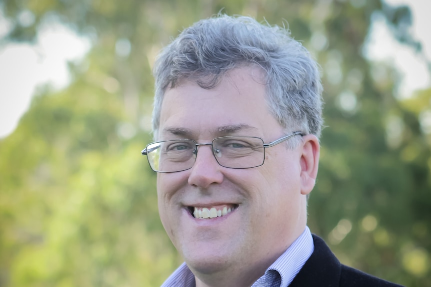 A smiling, grey-haired man wearing glasses and a suit