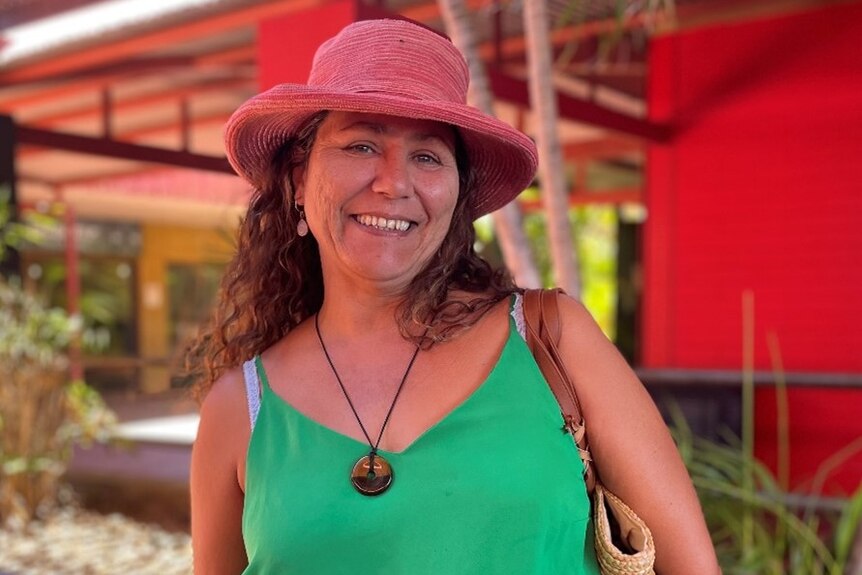 A woman wearing a hat and a green top smiles for a photo outdoors.