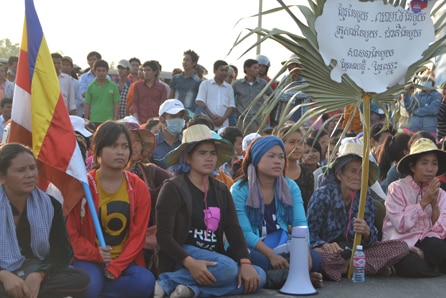 A group of Cambodians sit behind a flag and a sign while protesting.