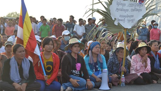 A group of Cambodians sit behind a flag and a sign while protesting.