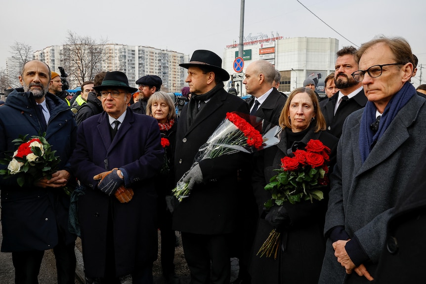 A crowd of people dressed in black holding roses. 