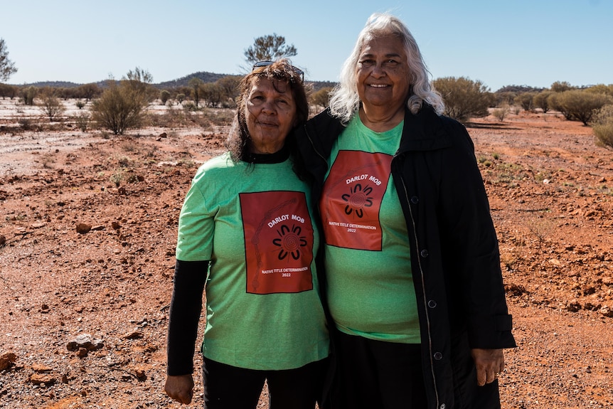 Two indigenous women on country standing arm-in-arm