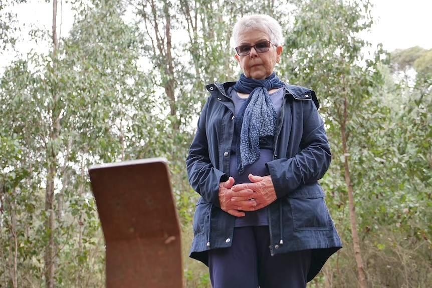 Senior woman stands at her husband's burial plot