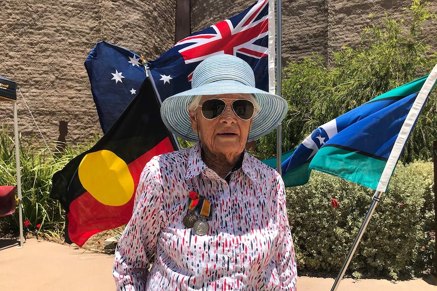 A lady with medals on her chest stand in front of flags in Winton