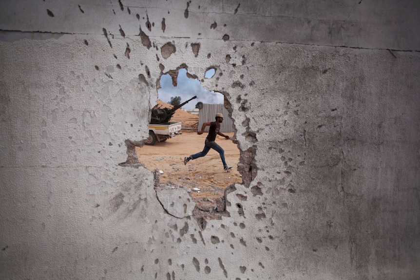 Though a hole from bullets in a wall, a man is seen running in Libya.