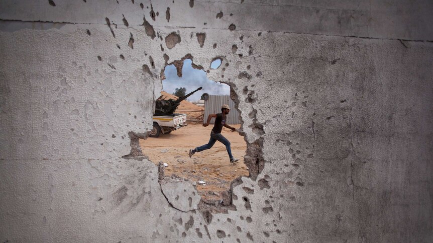 Though a hole from bullets in a wall, a man is seen running in Libya.