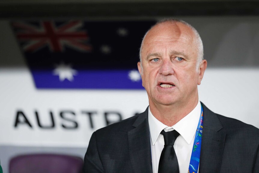 Graham Arnold stands wearing a suit with his mouth slightly open