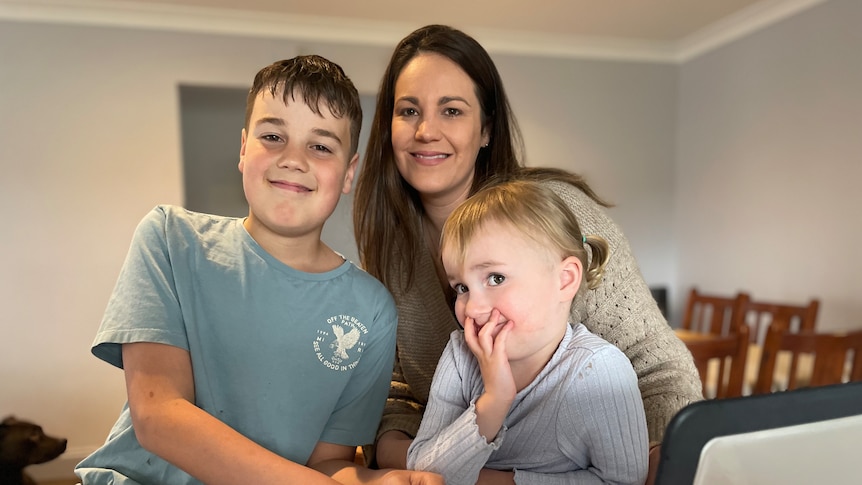 A young mother with brown hair sitting at a table with her two young kids