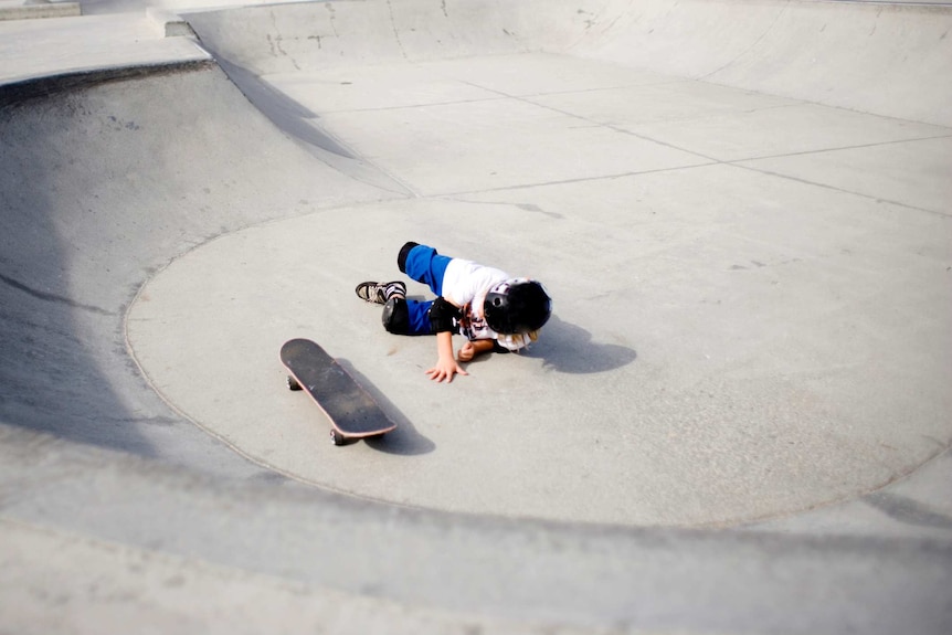 A young child on the ground after falling off their skateboard at a skatepark