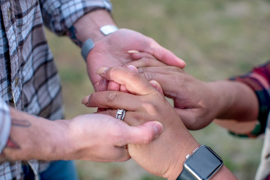 A man and a woman gently hold hands