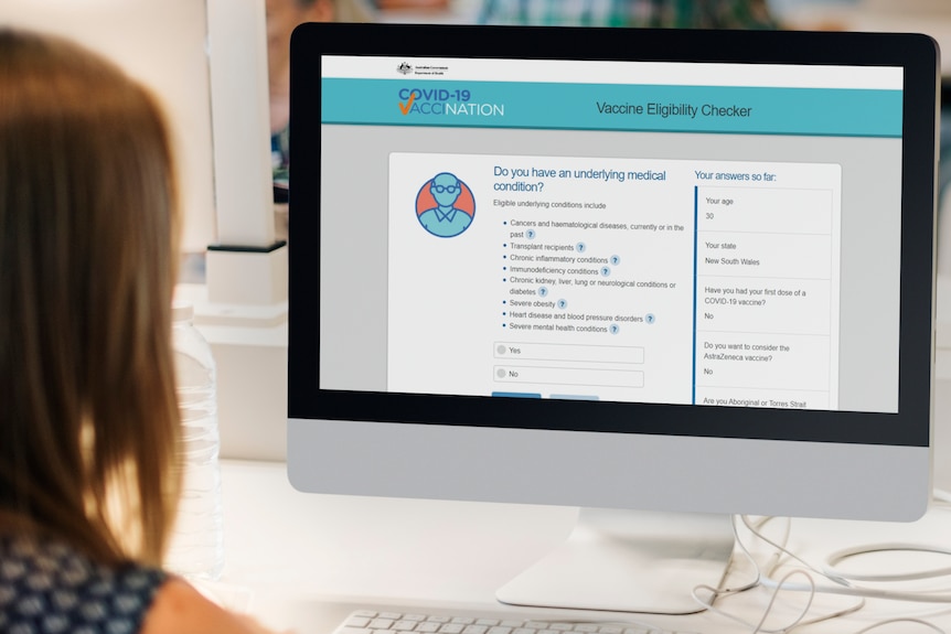 A woman sits at a computer displaying a website where people can answer questions to check their eligibility for a vaccine.