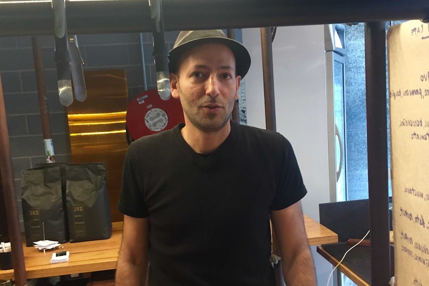 A man in black who is wearing a hat stands inside a Southbank cafe.