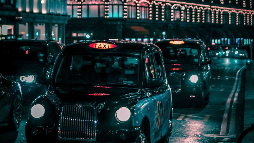 Illuminated buildings of Harrods in London viewed from a busy street with London cabs in the foreground.