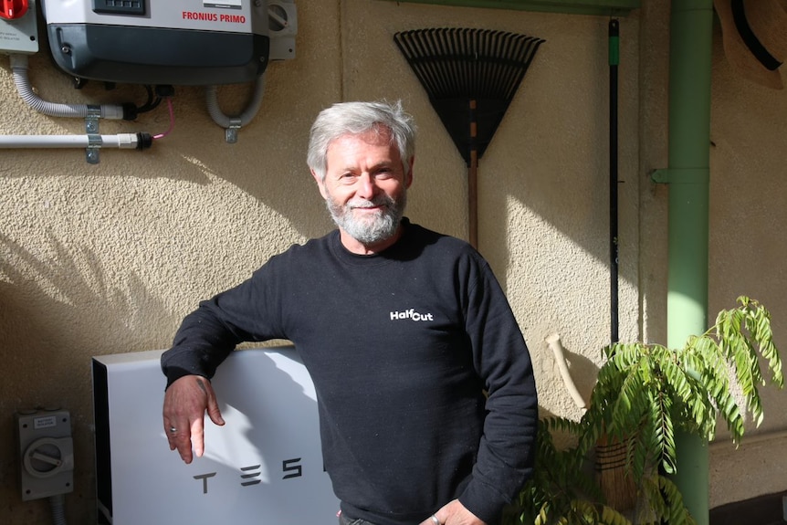 A man leans on a solar panel battery outside his home.