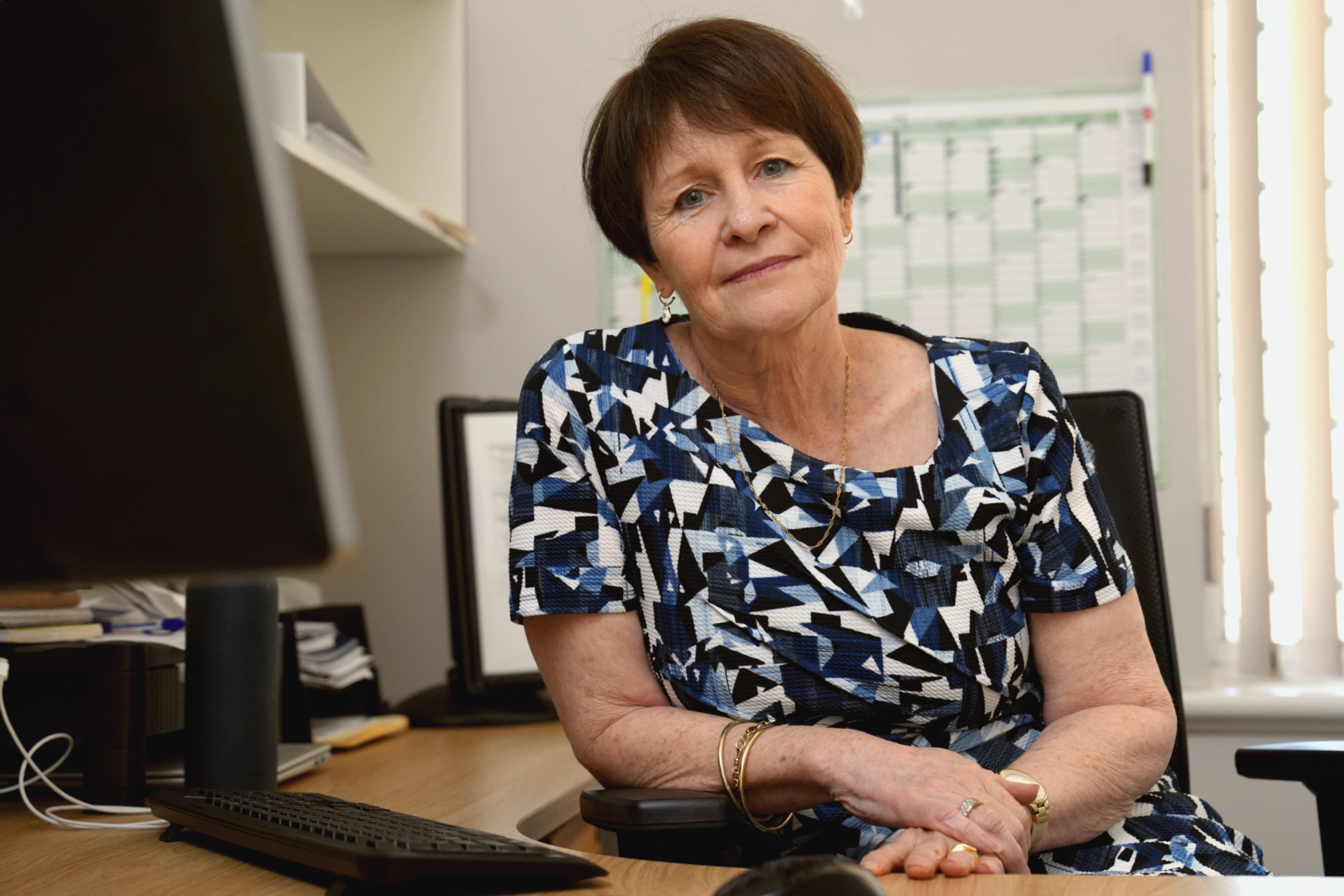 A woman sits at a desk with a sad smile.
