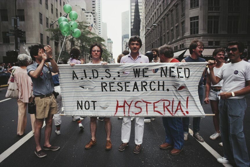 A group of men on a New York street hold a banner that says 'A.I.D.S: We need resrearch, not hysteria'.