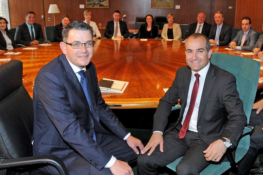 Two men wearing suits sit at a large round conference table.