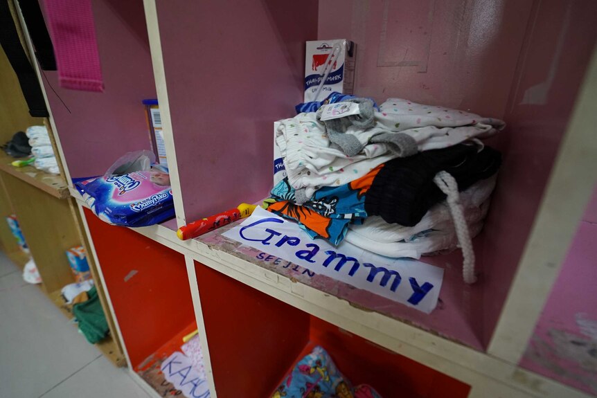 A pile of clothing and a milk carton sit in an open wooden kindergarten locker which is labelled "grammy"