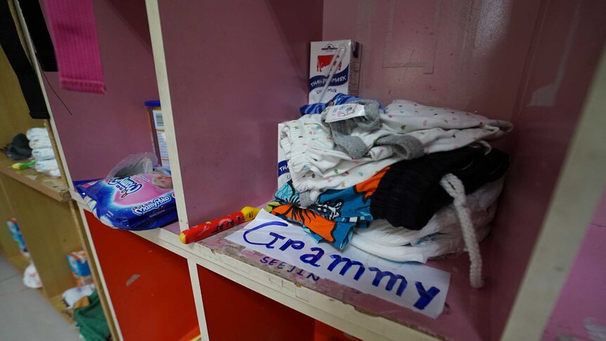 A pile of clothing and a milk carton sit in an open wooden kindergarten locker which is labelled "grammy"