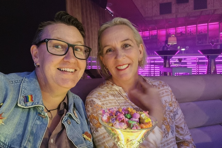 Two women in a pink lit bar with a bowl of rainbow popcorn.