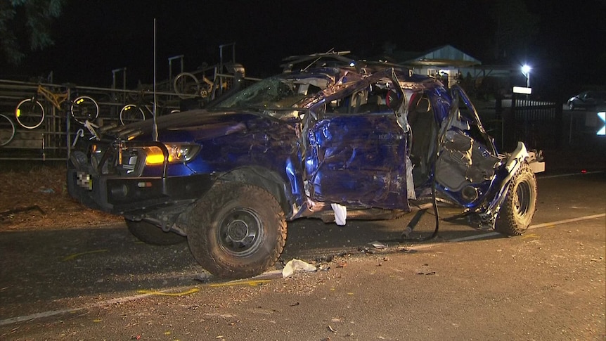 A badly damaged dark blue ute at night