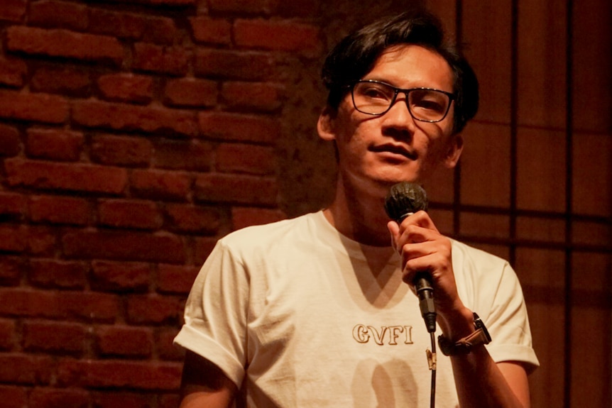 A man wearing glasses and holding a microphone on  a stage