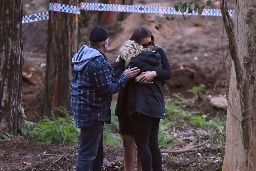 Three people embracing in forest.