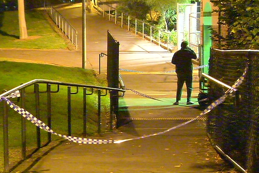A policeman stands with his back to the camera behind police tape at a train station.