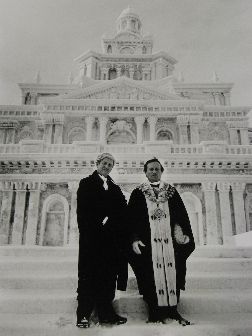 Two men, one in mayoral robes, stand in front of snow sculpture of Sydney Town Hall. Image is BW