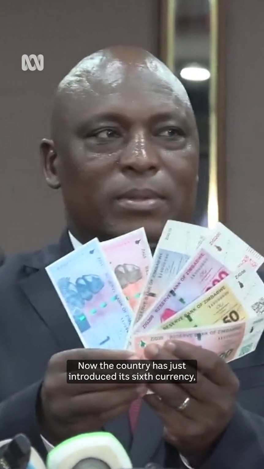 A Black man in a suit holds up a selection of colourful banknotes fanned out in front of him